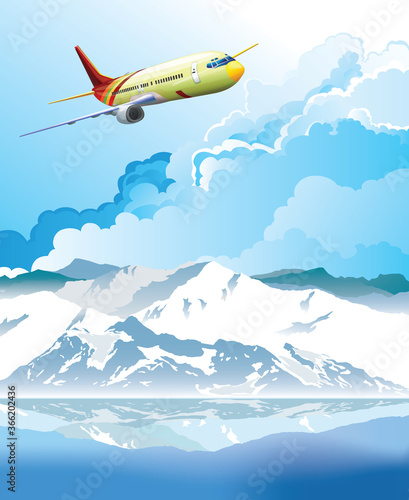 Passenger plane flying over snow capped mountain range reflected in foreground water set against a blue cloudy sky