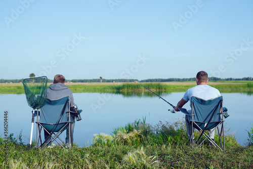 Two friends the Fishermans is sitting on a chairs by the lake and fishes.