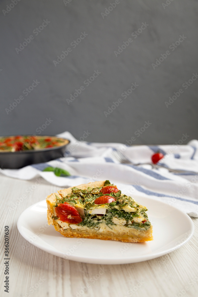 A Piece of Homemade Spinach Quiche on a white plate, side view. A Piece of Homemade Spinach Quiche on a white plate, side view.