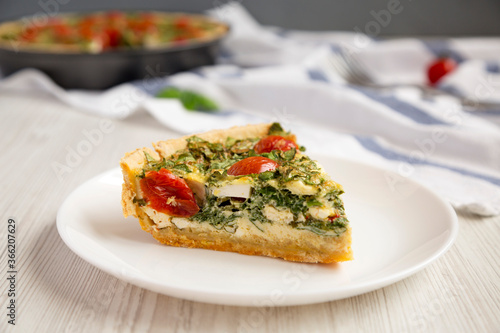 A Piece of Homemade Spinach Quiche on a white plate, low angle view.