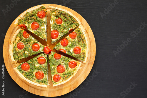Homemade Spinach Quiche on a round bamboo board on a black background, top view. Flat lay, overhead, from above. Copy space.