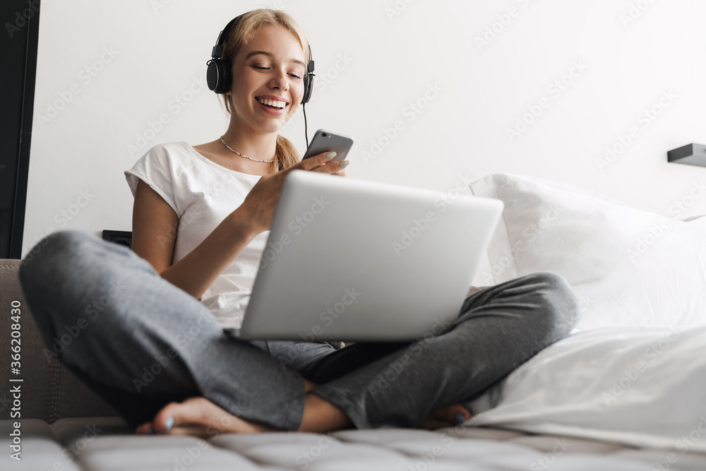 Photo of woman using headphones and cellphone while working with laptop Photo of woman using headphones and cellphone while working with laptop