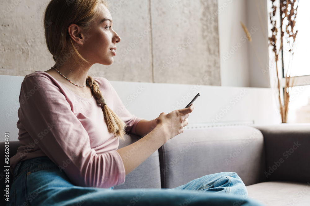 Photo of young beautiful woman using cellphone while sitting on sofa Photo of young beautiful woman using cellphone while sitting on sofa