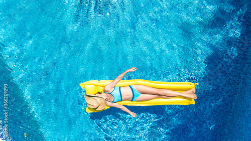 Girl relaxing in swimming pool, child swims on inflatable mattress and has fun in water on family vacation, tropical holiday resort, aerial drone view from above 