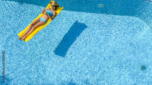 Beautiful young woman relaxing in swimming pool, girl swims on inflatable mattress and has fun in water on family vacation, tropical holiday resort, aerial drone view from above 