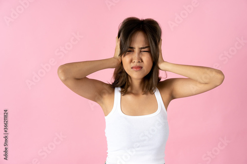 Frustrated young woman with eyes closed covering ears with hands against plain pink background © twinsterphoto