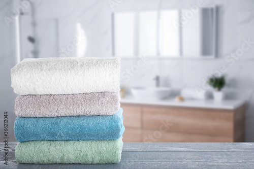 Stack of fresh towels on grey wooden table in bathroom. Space for text