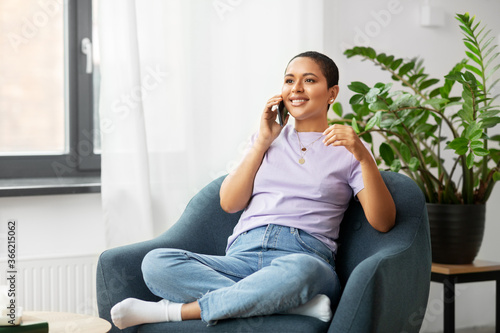 people, technology, communication and leisure concept - happy young african american woman calling on smartphone at home