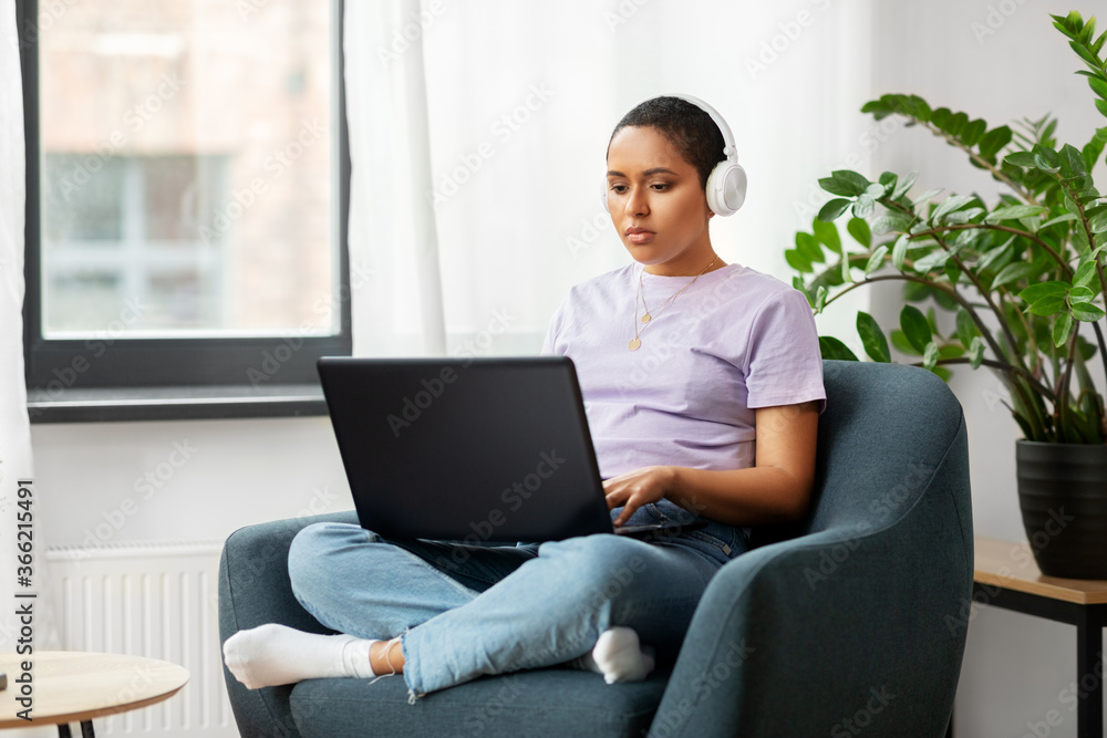 people, technology and leisure concept - young african american woman in headphones with laptop computer listening to music at home people, technology and leisure concept - young african american woman in headphones with laptop computer listening to music at home