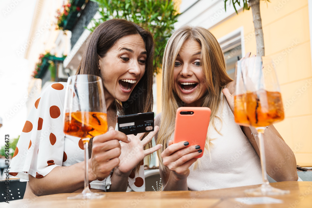 Image of women holding card and cellphone while drinking cocktails Image of women holding card and cellphone while drinking cocktails