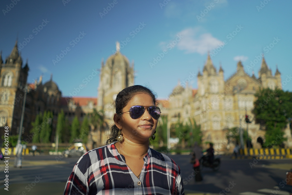 Obraz premium happy young woman in sunglasses. Young Indian Girl In front of Chhatrapati Shivaji Maharaj terminus (CSTM) Mumbai India