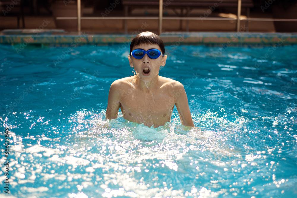 A little boy actively swims in the pool in the open air. The concept of sport and healthy lifestyle.