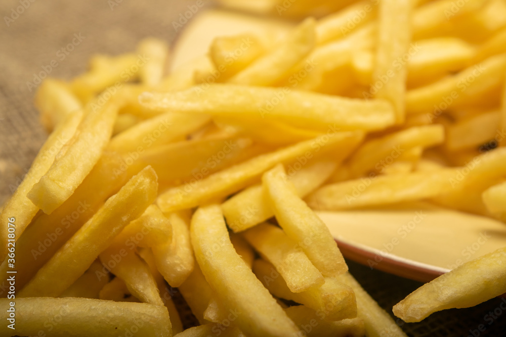 French fries in a round plate on a homespun cloth with a rough texture. Close up. French fries in a round plate on a homespun cloth with a rough texture. Close up.