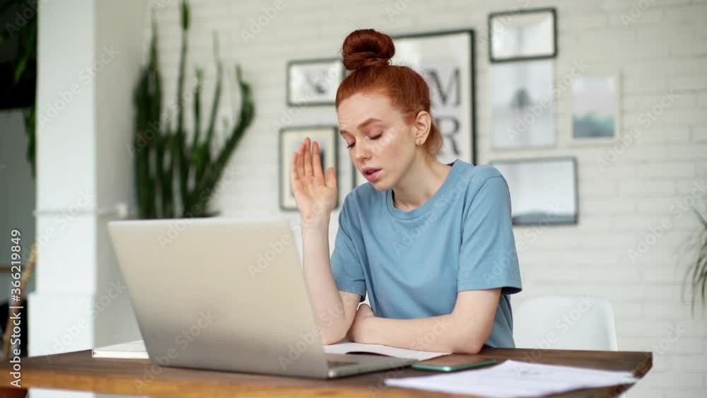 Tired young redhead woman is working on laptop computer at the desk in cozy room at home office. Girl freelancer is exhausted rubbing head and looking at screen. Concept of remote work or education. Tired young redhead woman is working on laptop computer at the desk in cozy room at home office. Girl freelancer is exhausted rubbing head and looking at screen. Concept of remote work or education.