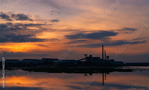 Landscape of factory industry buildings with dark blue and orange sunset sky reflection on water in the river. Warehouse building at night. Clean environment around factory. Factory closed.