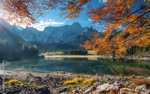 Impressive sunny autumn landscape of mountains. Beautiful natural scenery in Julian Alps. Scenic image of fairy-tale lake during sunset. Majestic Rocky Mountains on background. Fusine lake. Italy,