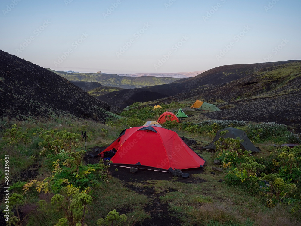 ICELAND, LANDMANNALAUGAR, August 2, 2019: Colorful tents in Botnar campsite at Iceland on Laugavegur hiking trail, green valley in volcanic landscape among lava fields with view on Myrdalsjokull