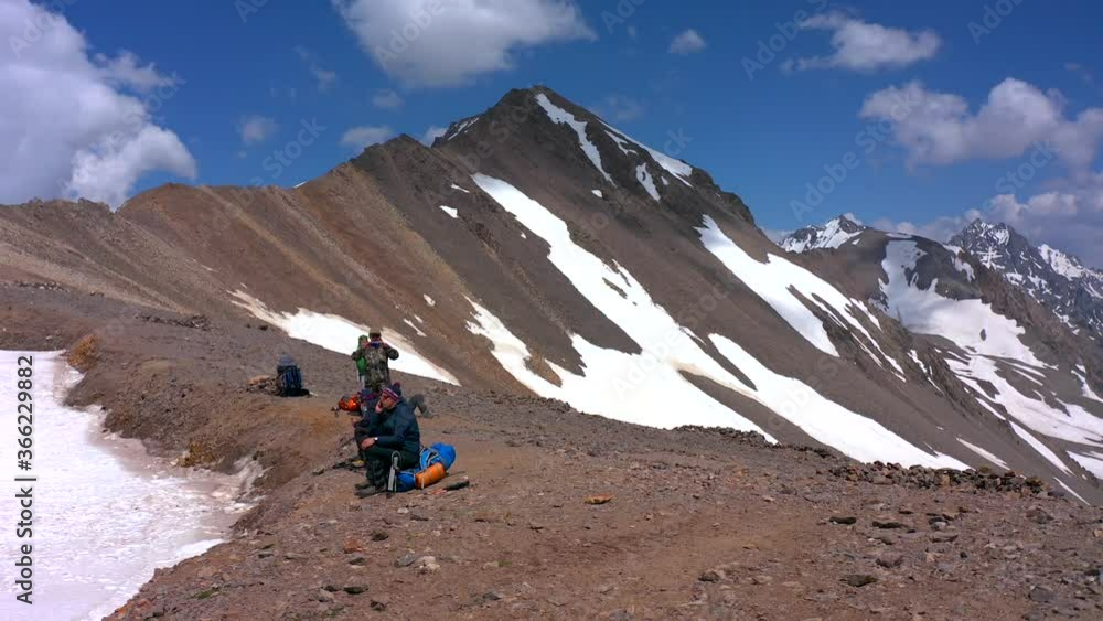 Five climbers with large backpacks are resting in front of Mount Elbrus. Aerial view of a beautiful mountain winter landscape. Snow-covered rocky slopes of the northern Elbrus region. Five climbers with large backpacks are resting in front of Mount Elbrus. Aerial view of a beautiful mountain winter landscape. Snow-covered rocky slopes of the northern Elbrus region.