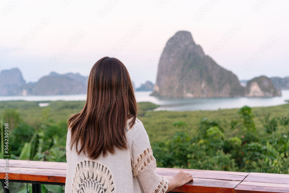Young Asian traveller woman sit and see the mountain in early morning at the Sametnangshe Island viewpoint, Phang-Nga, Thailand.
