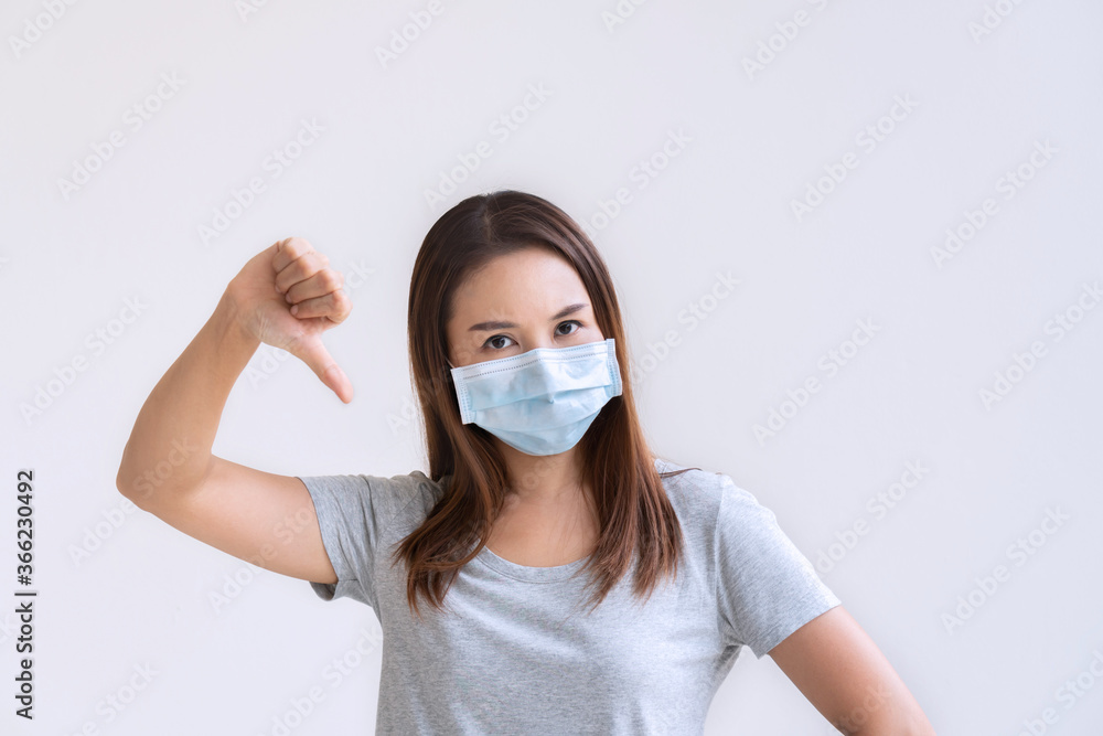 Portrait of unhappy young Asian girl with protective face mask thumb down posing over white background. Copy space Portrait of unhappy young Asian girl with protective face mask thumb down posing over white background. Copy space