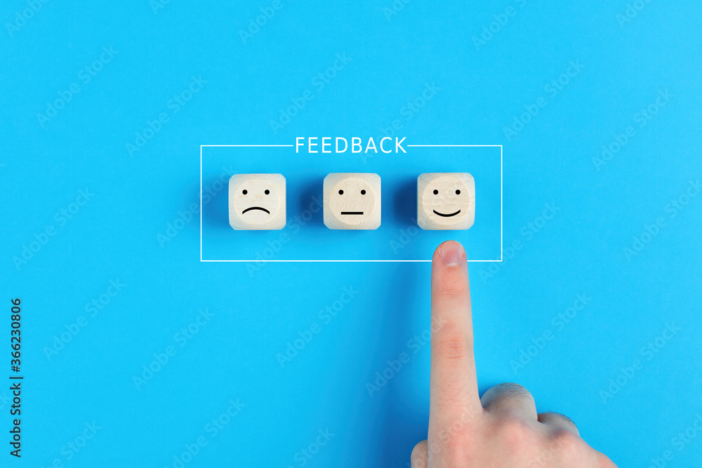 Fototapeta premium Male hand chooses the happy face among unhappy faces on wooden blocks. Concept of customer satisfaction or positive feedback.