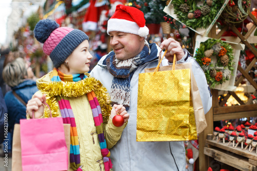Happy friendly family of father and teen daughter holding bags after shopping on Christmas market