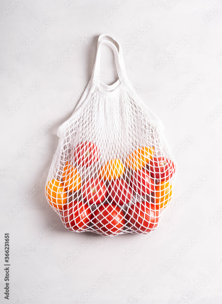 Eco-friendly mesh bag with tomatoes on a gray surface, flat lay, top view. Zero waste, no plastic concept.