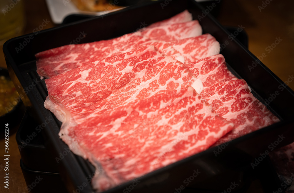 Raw sliced Wagyu beef for shabu shabu on black tray in the restaurant.