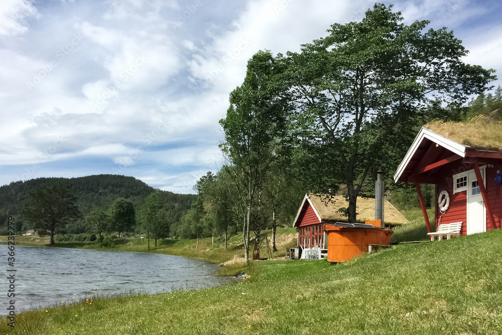 Obraz premium red wooden houses with a grass roof in the Scandinavian style on the lake