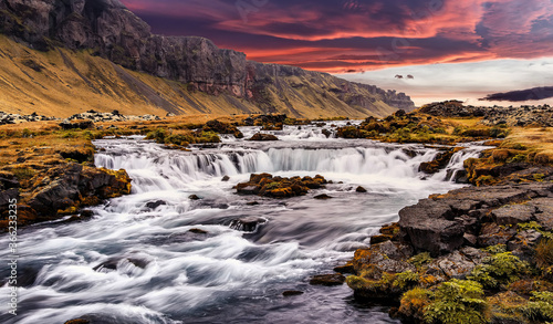 Wonderful nature of Iceland. fresh green grass and icelandic moss near river with waterfall. Tipical Icelandic scenery during sunset. Dramatic Scene of powerfull Waterfall with colorful sky