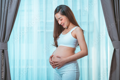 close up pregnant woman in a White underwear, posing Belly of a pregnant woman. smile happy Posing side view standing beside curtain in bedroom her