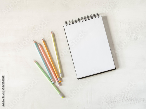 Fototapeta Naklejka Na Ścianę i Meble -  Blank sheet notebook with copy space for text and multicolored graphite pencils on white background. Flat lay, top view girl work business concept for lifestyle blog