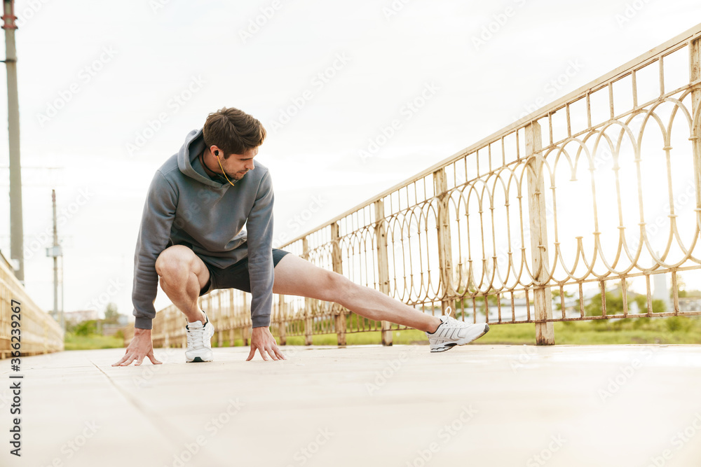 Image of young sportsman in earphones doing exercise while working out