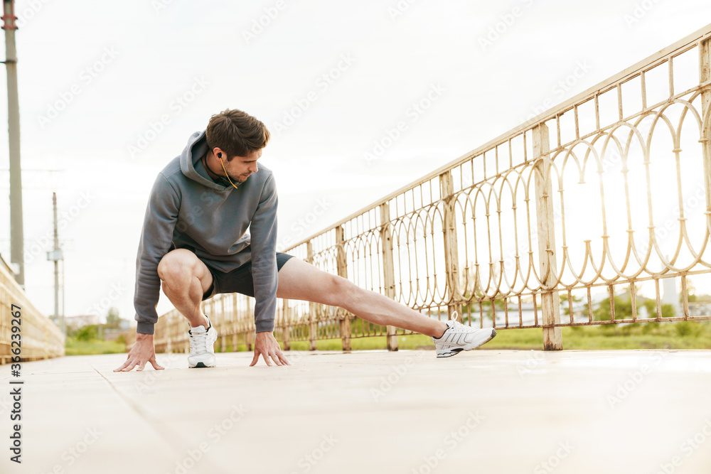 Image of young sportsman in earphones doing exercise while working out Image of young sportsman in earphones doing exercise while working out