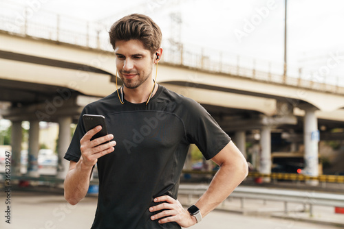 Image of pleased young sportsman using cellphone while working out
