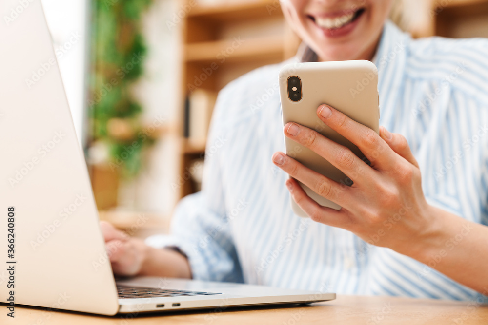 Cropped image of woman typing on mobile phone while working with laptop Cropped image of woman typing on mobile phone while working with laptop