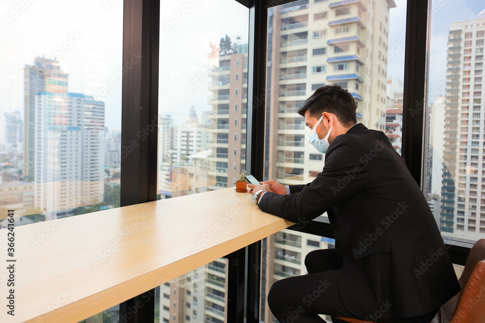 Fototapeta premium Caucasian businessman wearing facial mask dressing in formal wear making a using cellphone in the modern urban business office with skyscraper during new normal and social distancing policy