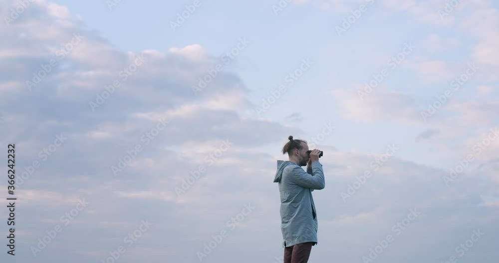 Airy low angle view of man birdwatching in binoculars on blue sky background copy text space. Stylish explorer traveler looking into glass look-see outdoors handheld device. Travel vacation naturalist Airy low angle view of man birdwatching in binoculars on blue sky background copy text space. Stylish explorer traveler looking into glass look-see outdoors handheld device. Travel vacation naturalist