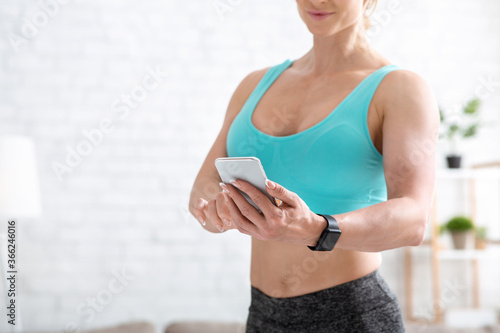 Online trainer tips. Adult woman in sportswear with fitness tracker typing on smartphone