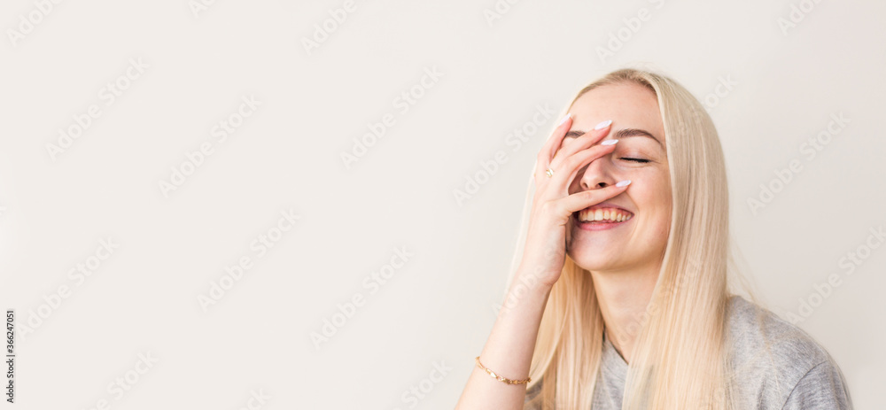 Vivacious woman giglling with her eyes screwed up in a moment of fun as she sitting against beige studio wall. Happy natural laughing young casual female covering mouth. Human face expressions Vivacious woman giglling with her eyes screwed up in a moment of fun as she sitting against beige studio wall. Happy natural laughing young casual female covering mouth. Human face expressions