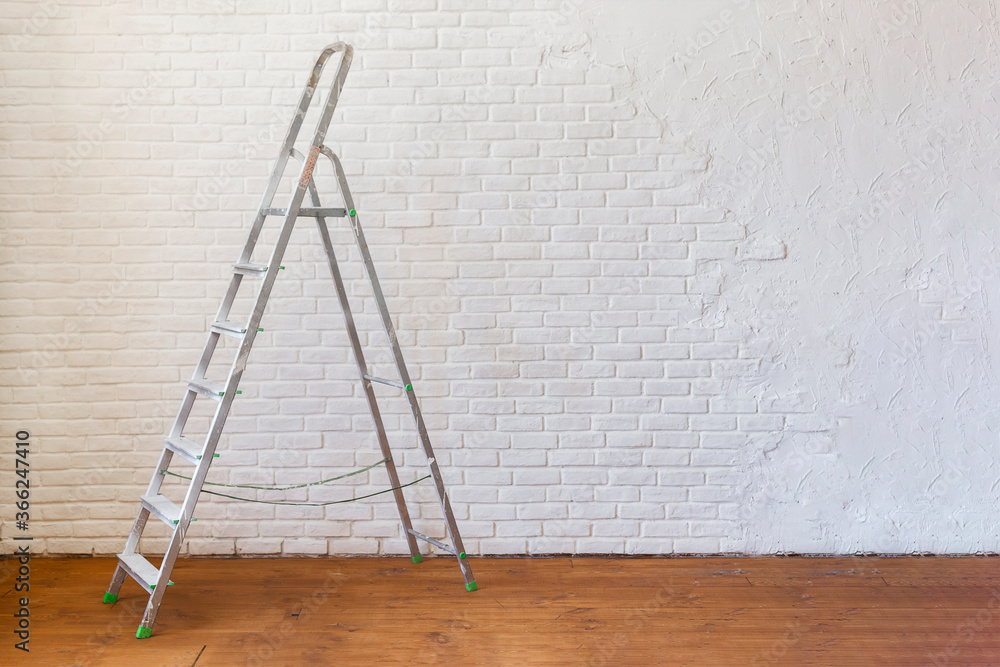 A construction ladder stands on a wooden floor. - obrazy, fototapety, plakaty 
