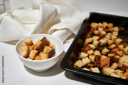 Square toasted pieces of homemade delicious rusk, hardtack, Dryasdust, zwieback on a white plate and baking sheet.