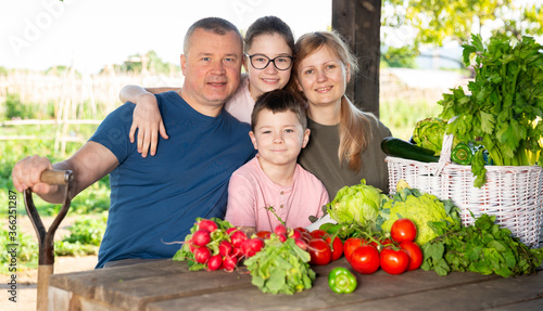 Portrait of happy friendly family resting at wooden table in summer gazebo after harvesting in home garden.