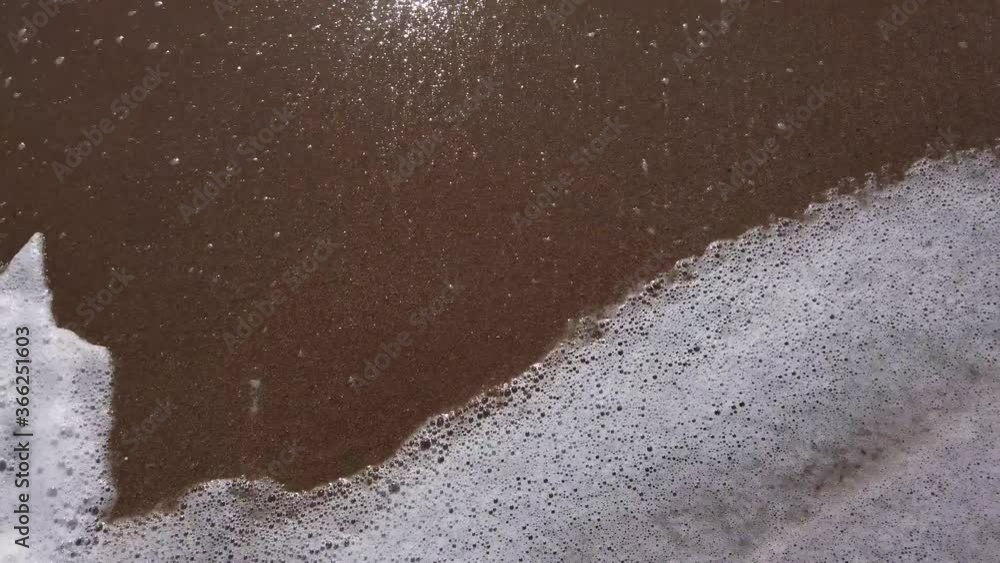 Slow motion video. A white foamy wave runs onto a golden sandy shore. Travel concept. Top view, viewing point of a person standing on a sandy beach. Slow motion video. A white foamy wave runs onto a golden sandy shore. Travel concept. Top view, viewing point of a person standing on a sandy beach.