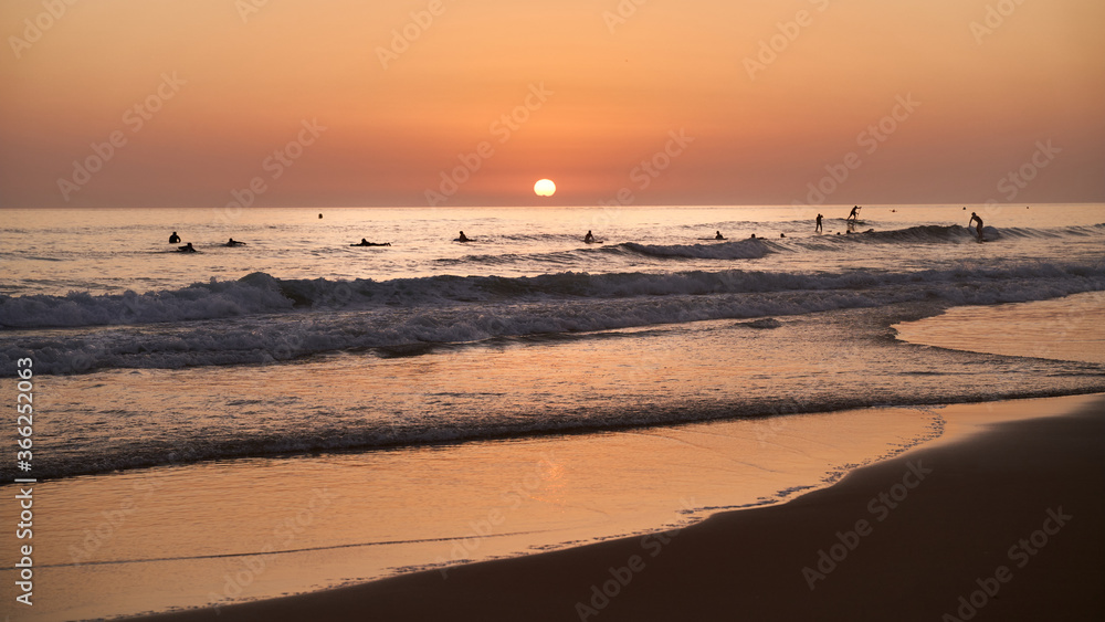 Sunset on the beach of Cadiz (Spain) with the sun in the background and surfers in the water. Concept of beach, vacation and travel.