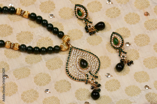 Indian traditional jewelry placed on cloth with earrings.diamond and green stone pendant,Luxury female jewelry, Indian traditional jewellery, diamond earring,Bridal Gold wedding jewellery