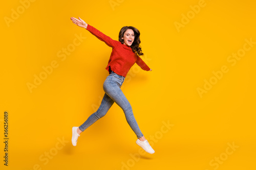 Fototapeta Naklejka Na Ścianę i Meble -  Full body photo of attractive pretty lady jumping high up spread arms like wings plane flight walking street crazy wear red sweater jeans shoes isolated yellow color background