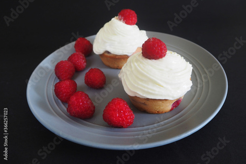 raspberries and two gluten-free cupcakes with mascarpone cream and cream on a gray round plate on a black background