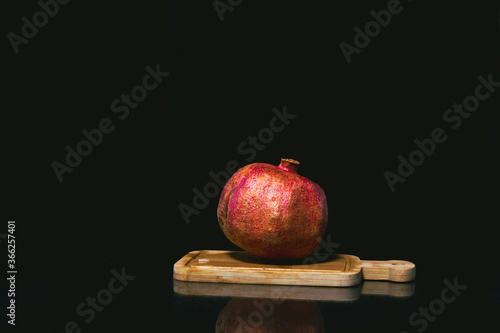 Pomegranate on a board on a dark background, reflection