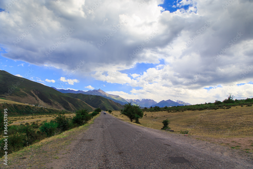 Beautiful summer landscape. Mountain country road among green hills. Lush green hills, high mountains. Spring flowering grass.
